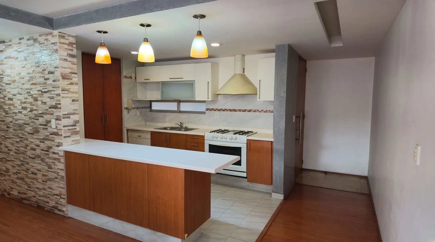 Cocina integral con barra, muro de piedra y lámparas colgantes